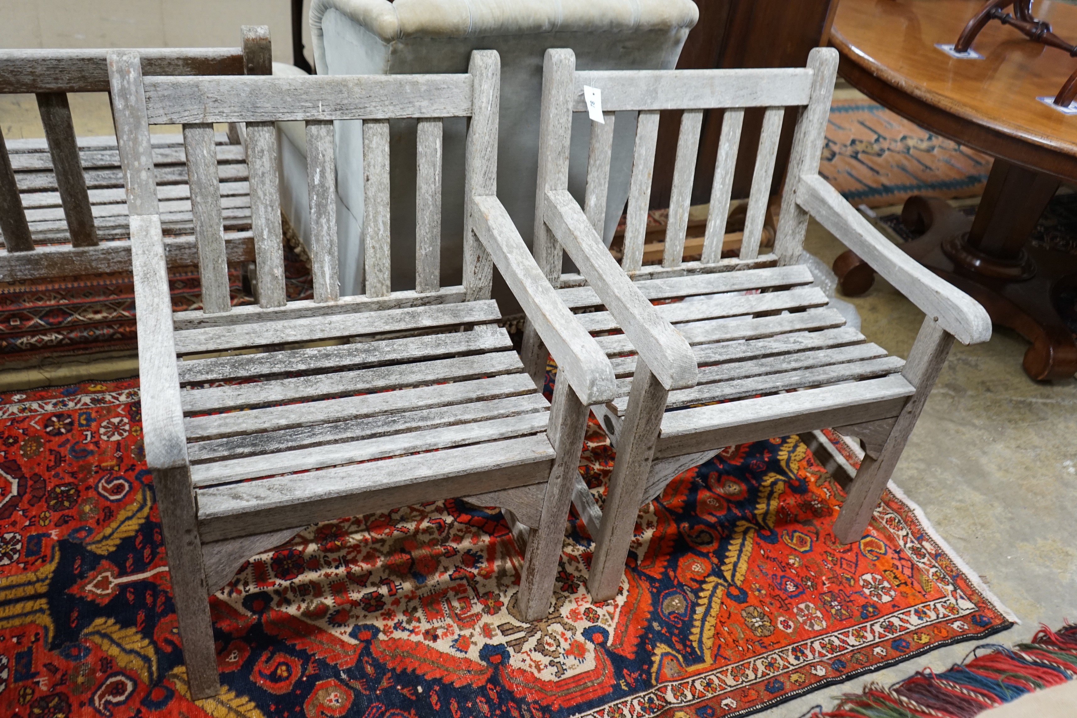 A pair of slatted weathered teak garden elbow chairs, width 60cm, depth 58cm, height 83cm